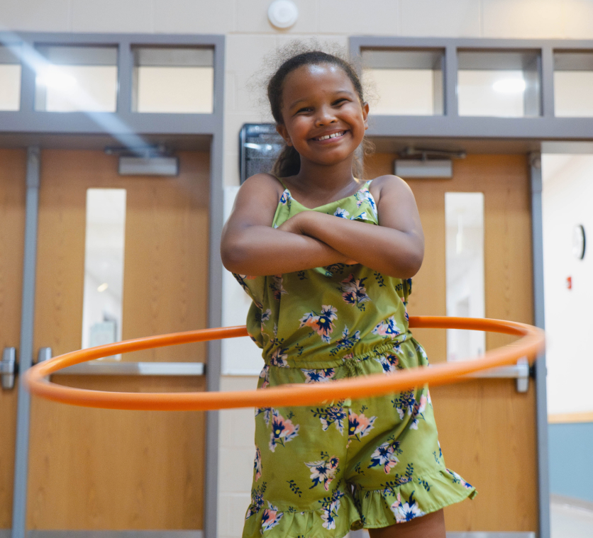A girl smiles while spinning a hula hoop.